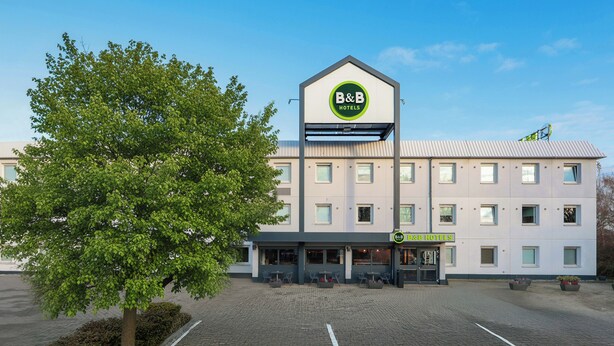 A B&B hotel with a modern design, a parking lot, and a large tree in front. - Ibis Budget Berlin Genshagen (Ludwigsfelde)