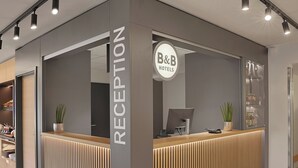 A reception desk with a modern design, a sign indicating it's for B&B Hotels, and a computer monitor. - Ibis Budget Berlin Genshagen (Ludwigsfelde)