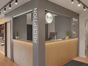 Uma receção com design moderno, placa indicando ser de B&B Hotels e um monitor de computador.