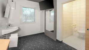 A modern bathroom with a sink, mirror, and shower area. - Ibis Budget Berlin Genshagen (Ludwigsfelde)