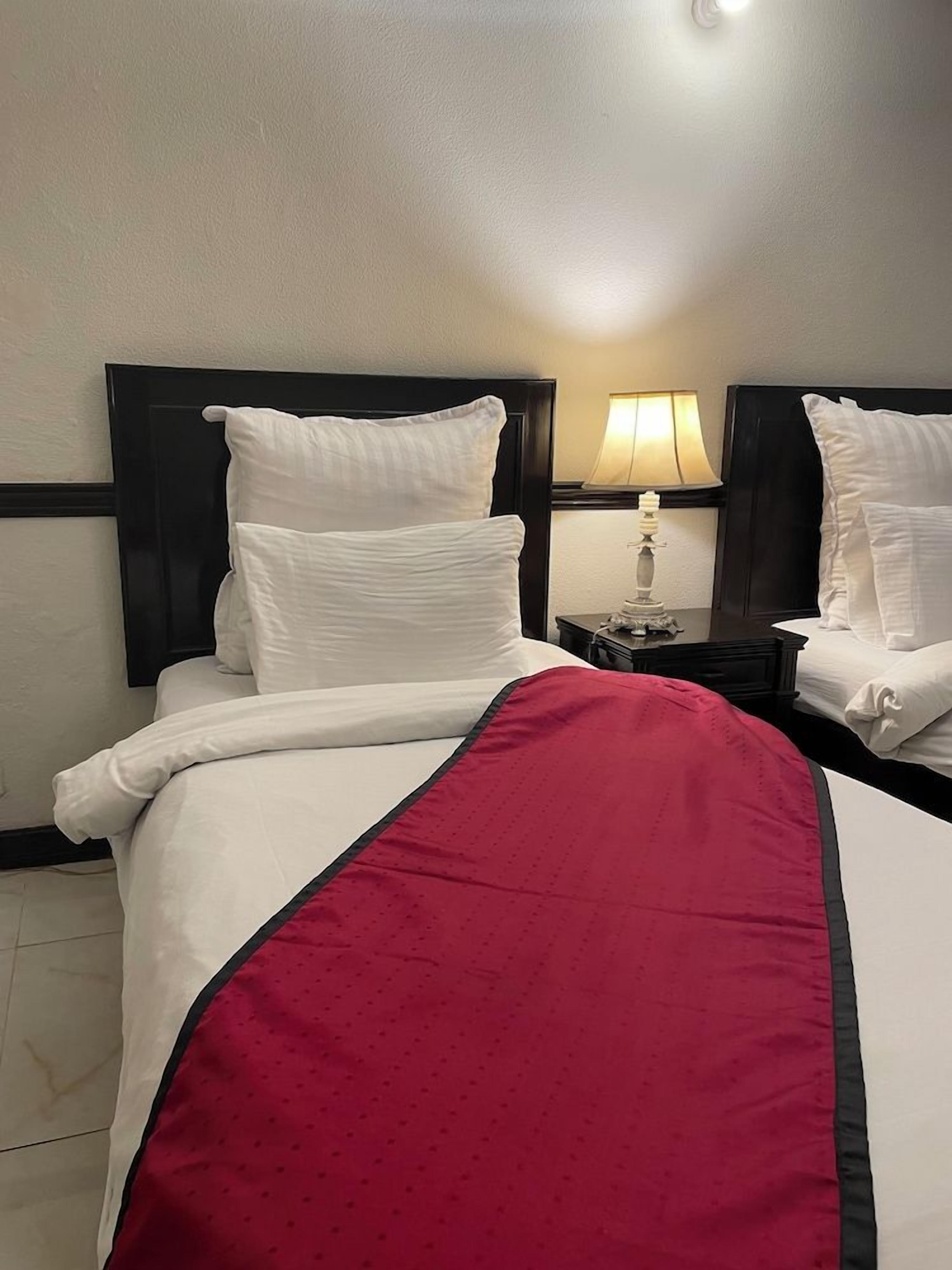 Une chambre d’hôtel avec un lit, une table de chevet avec une lampe et un plaid rouge.