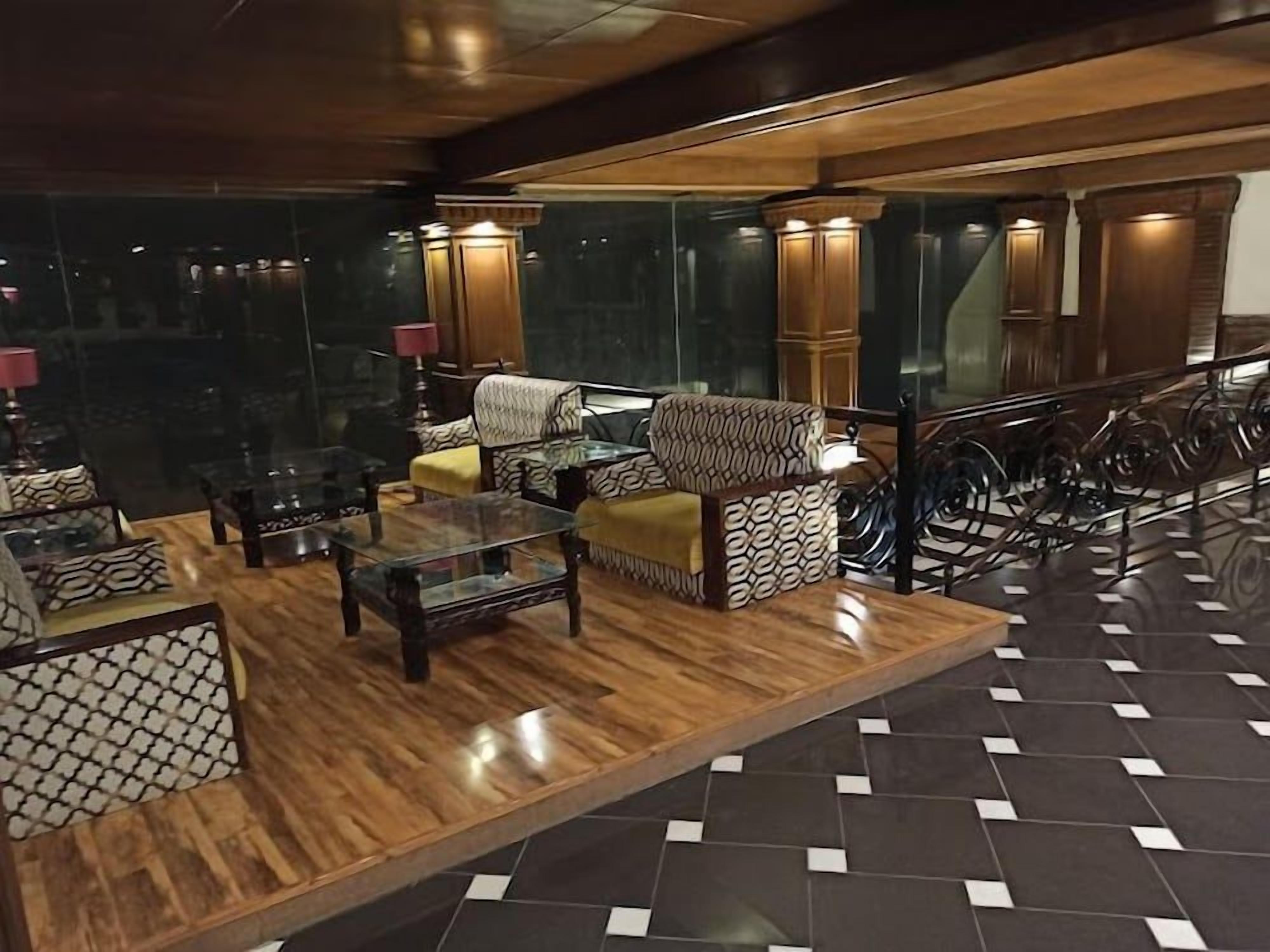A hotel lobby with a wooden reception desk, seating area with patterned sofas, and a staircase.