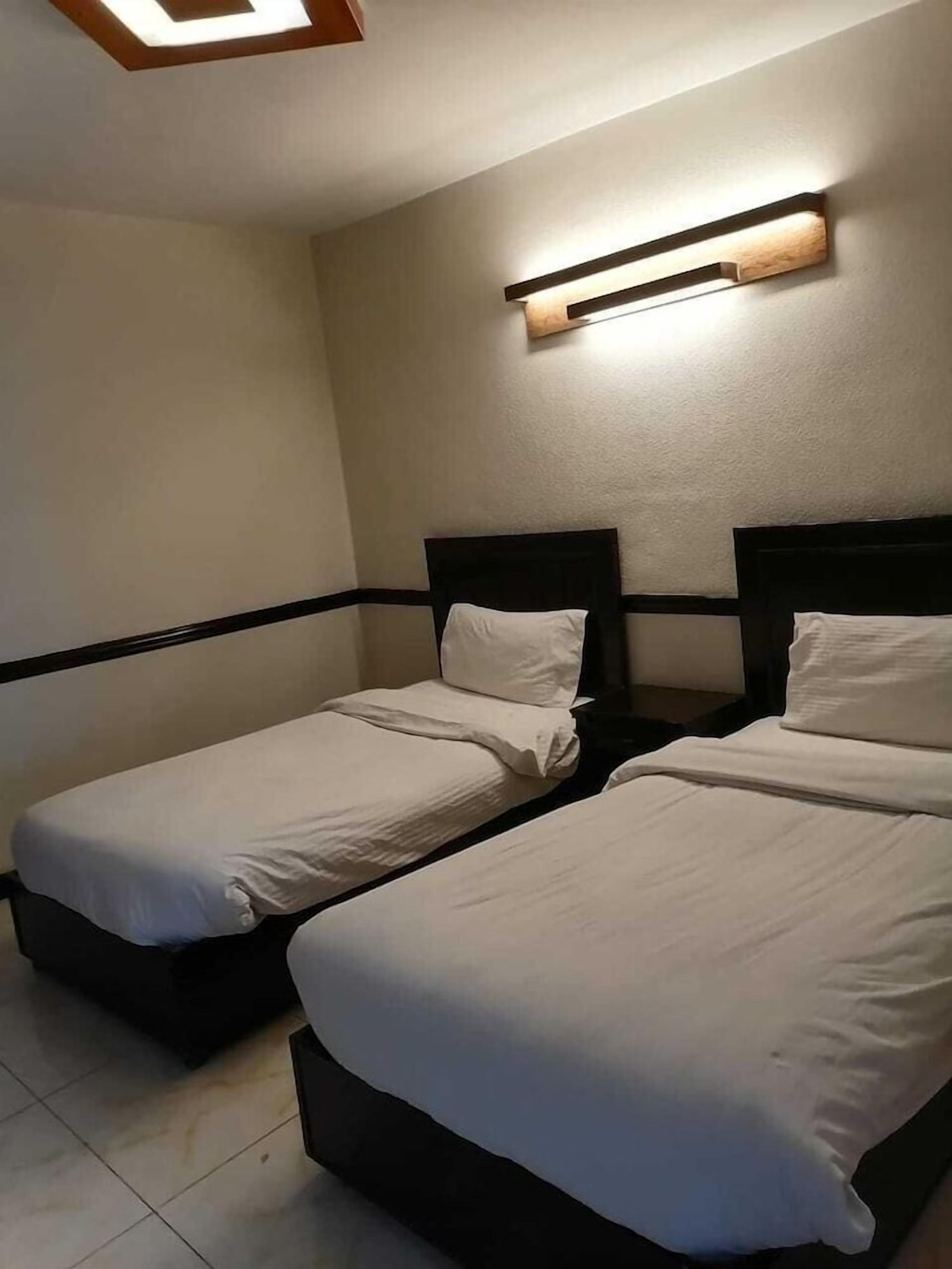 Habitación de hotel con dos camas individuales, una mesita de noche y un aplique de pared.