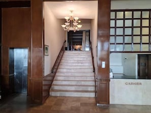 A staircase leading to a lobby area with a chandelier, a cash register, and a view of the interior space.