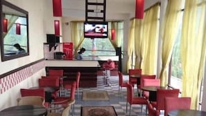 A restaurant with checkered flooring, red and beige chairs, a central rug, and a TV screen. - Shangrila Hotel & Resort Changla Gali (Abbottabad)
