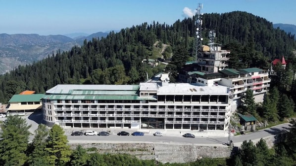 Ein mehrstöckiges Hotel mit Parkplatz, umgeben von bewaldeten Hügeln.