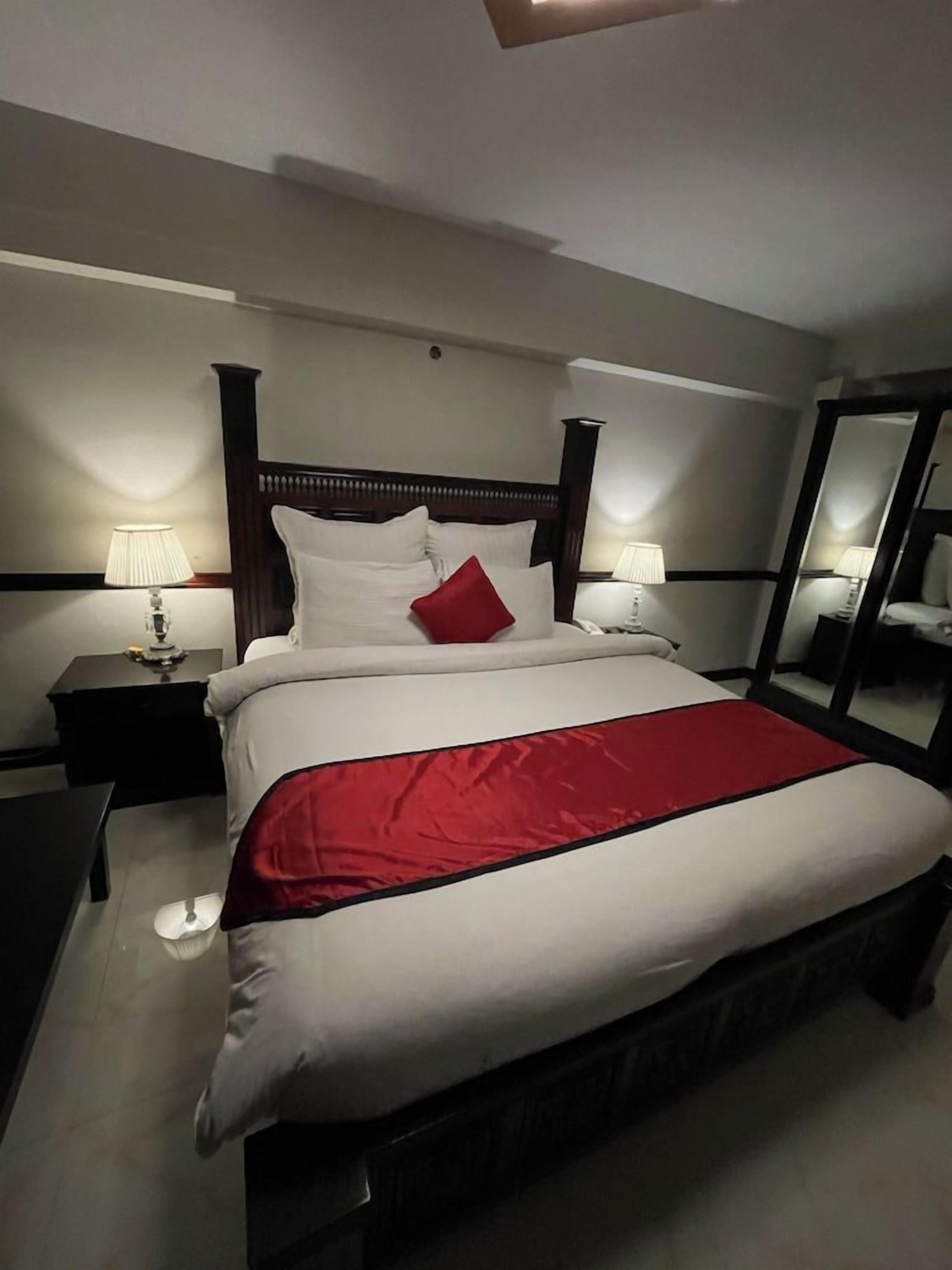 A hotel room with a large bed, two bedside tables, a mirror, and a lamp.