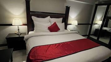A hotel room with a large bed, two bedside tables, a mirror, and a lamp.