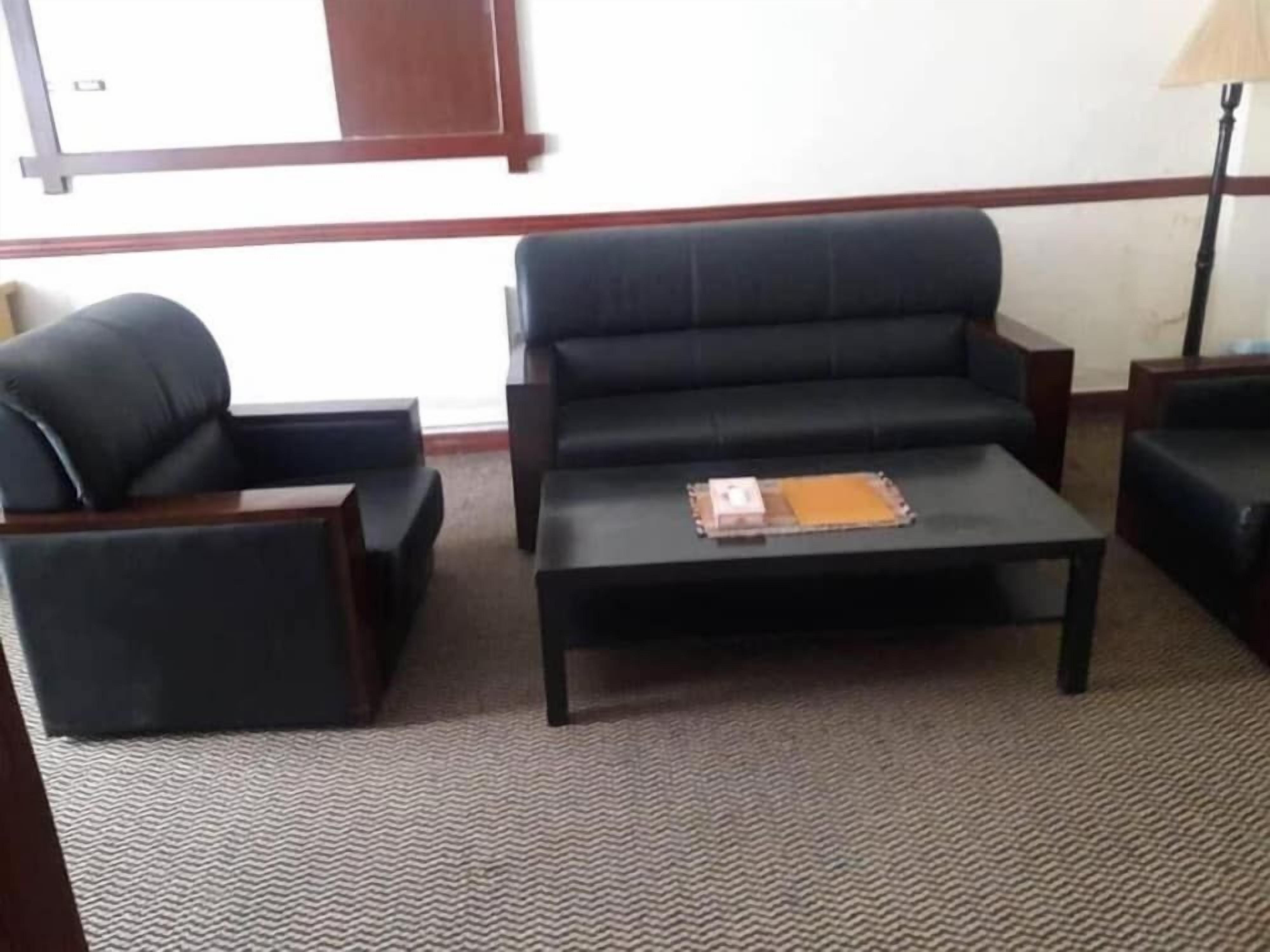 Una habitación con un sofá negro, un sillón a juego y una mesita con un libro y una carpeta.