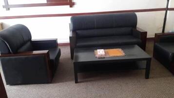 Una habitación con un sofá negro, un sillón a juego y una mesita con un libro y una carpeta.