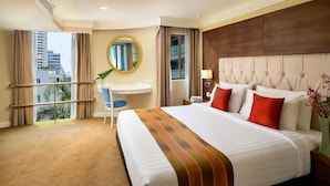 A hotel room with a large bed, a desk, a chair, a round mirror, and a view of the city through the window. - Court Wing Hotel Sukhumvit Bangkok (Bangkok)