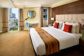A hotel room with a large bed, a desk, a chair, a round mirror, and a view of the city through the window. - Court Wing Hotel Sukhumvit Bangkok (Bangkok)