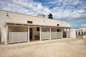 A building with a covered outdoor area, a gravel ground, and a gate.