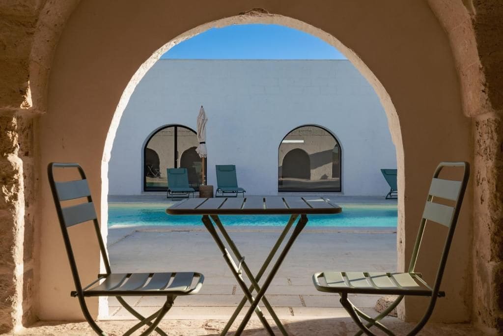 Ein Sitzbereich im Freien mit Pool, zwei Stühlen und einem Tisch, eingebettet in einer Bogenstruktur.