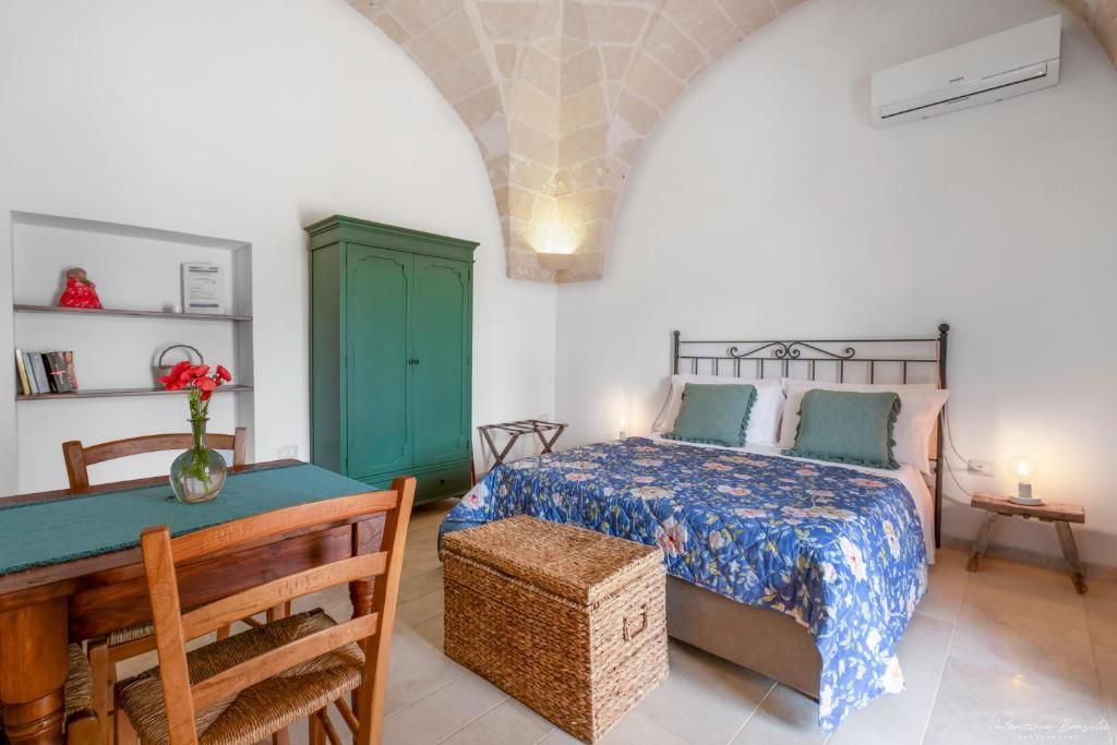 Un dormitorio con cama, una mesa de madera con sillas, un armario verde y una mesita de noche con lámpara.