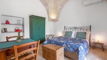 Un dormitorio con cama, una mesa de madera con sillas, un armario verde y una mesita de noche con lámpara.