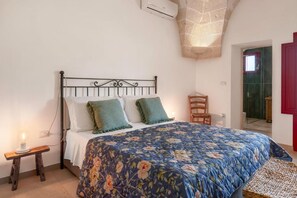 A bedroom with a bed, a bedside table with a lamp, a chair, and a red door. - Masseria Rescio (Avetrana)