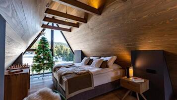 A cozy bedroom with a sloped ceiling, a bed, a nightstand, a small table, and a Christmas tree.