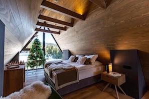 Un dormitorio acogedor con techo inclinado, una cama, una mesita de noche, una pequeña mesa y un árbol de Navidad.