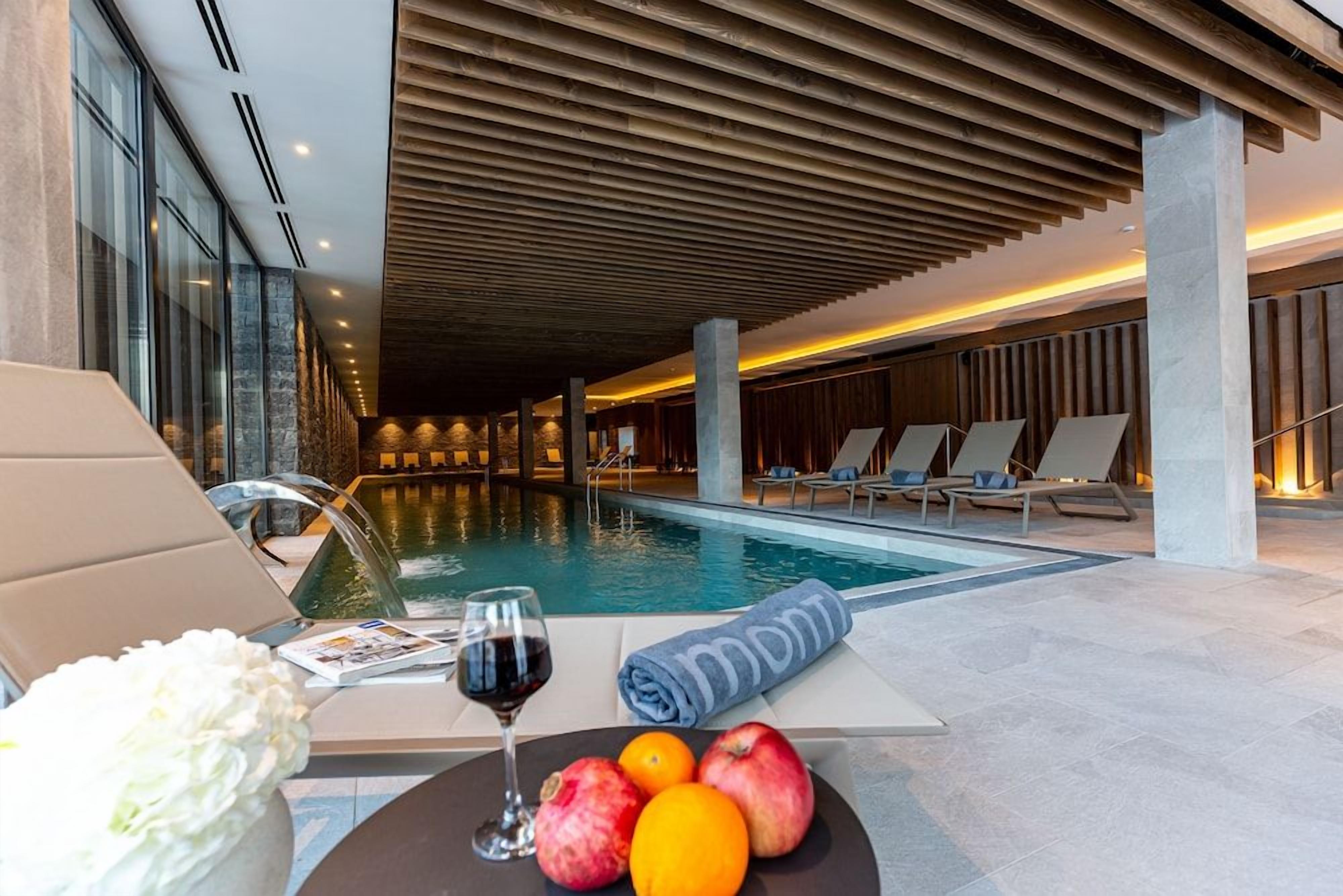 A poolside area with lounge chairs, a table with fruits and a glass of wine, and a towel with a logo.