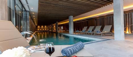 A poolside area with lounge chairs, a table with fruits and a glass of wine, and a towel with a logo.