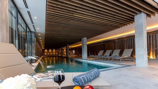 A poolside area with lounge chairs, a table with fruits and a glass of wine, and a towel with a logo. - Monti Spa Wellness Hotel Igman (Hadzici)