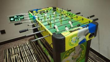 Una mesa de fútbol de mesa con un esquema de color verde y amarillo, un cartel indicador en la pared y una alfombra estampada.