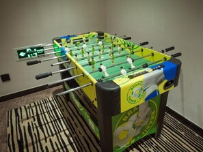 Una mesa de fútbol de mesa con un esquema de color verde y amarillo, un cartel indicador en la pared y una alfombra estampada.