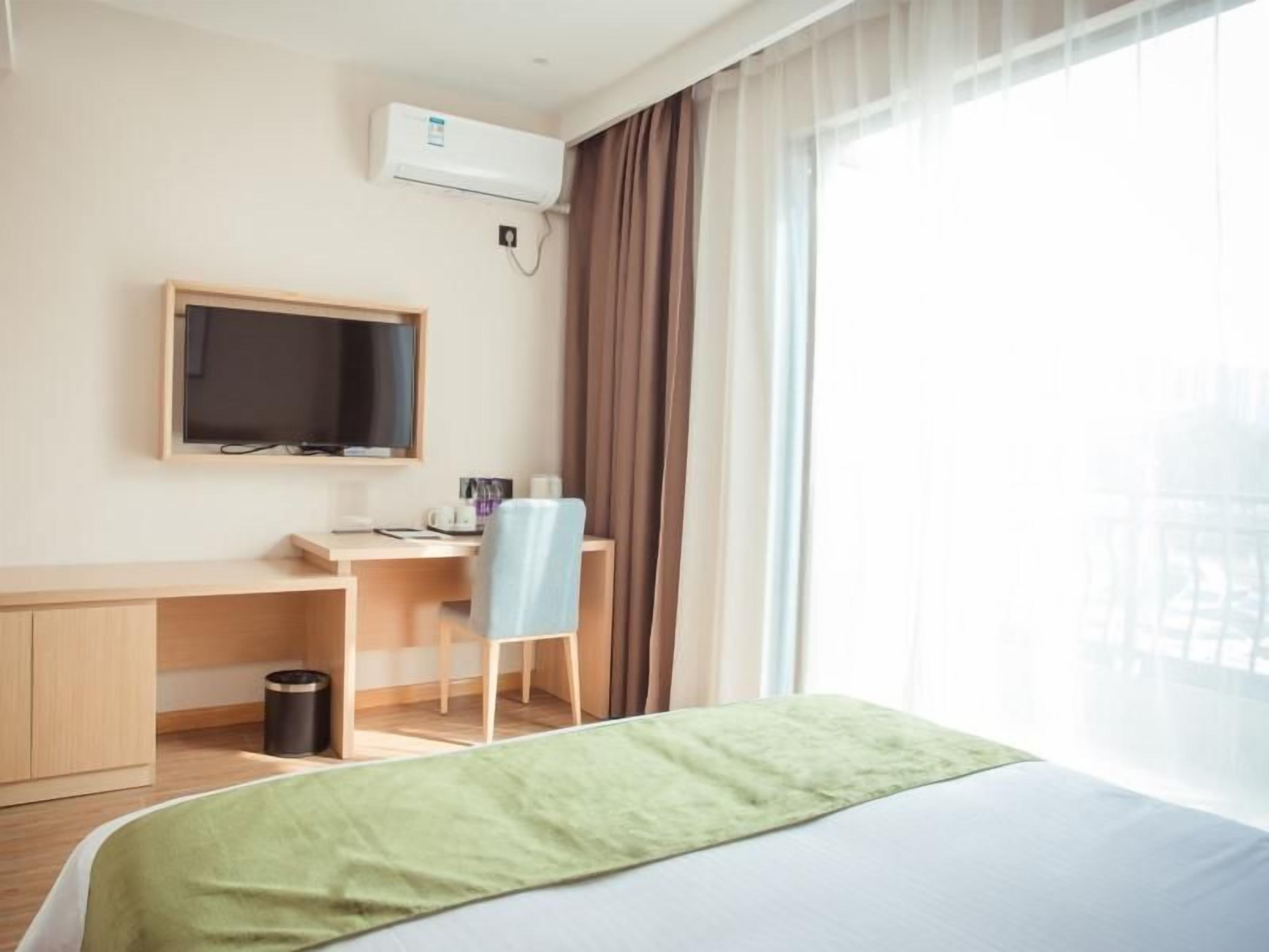 Una habitación de hotel con cama, escritorio, silla, televisor y ventana con cortinas.