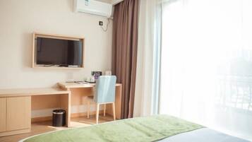 Una habitación de hotel con cama, escritorio, silla, televisor y ventana con cortinas.