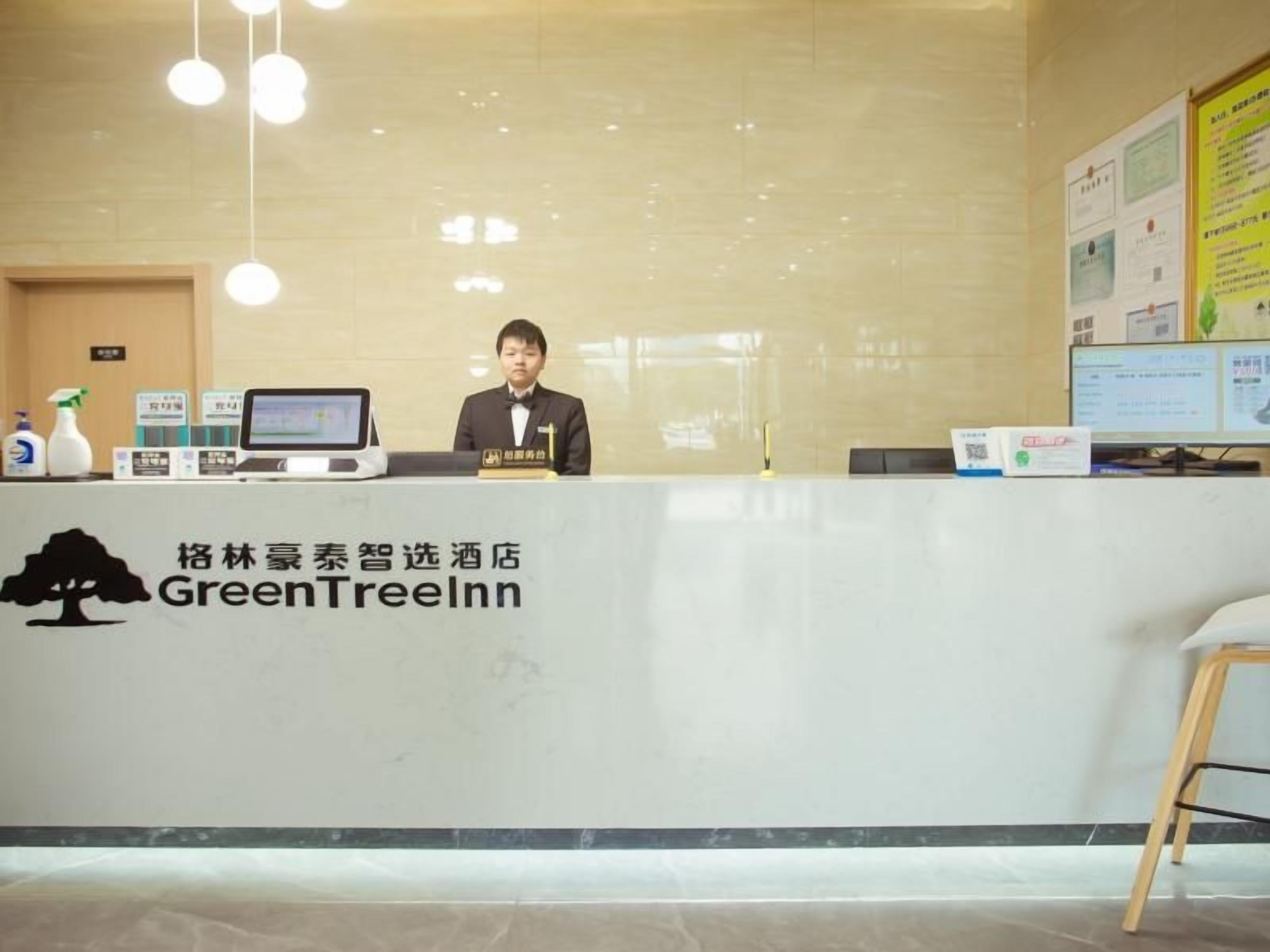 Un mostrador de recepción de hotel con una computadora, un cartel con el nombre del hotel y una silla de madera.
