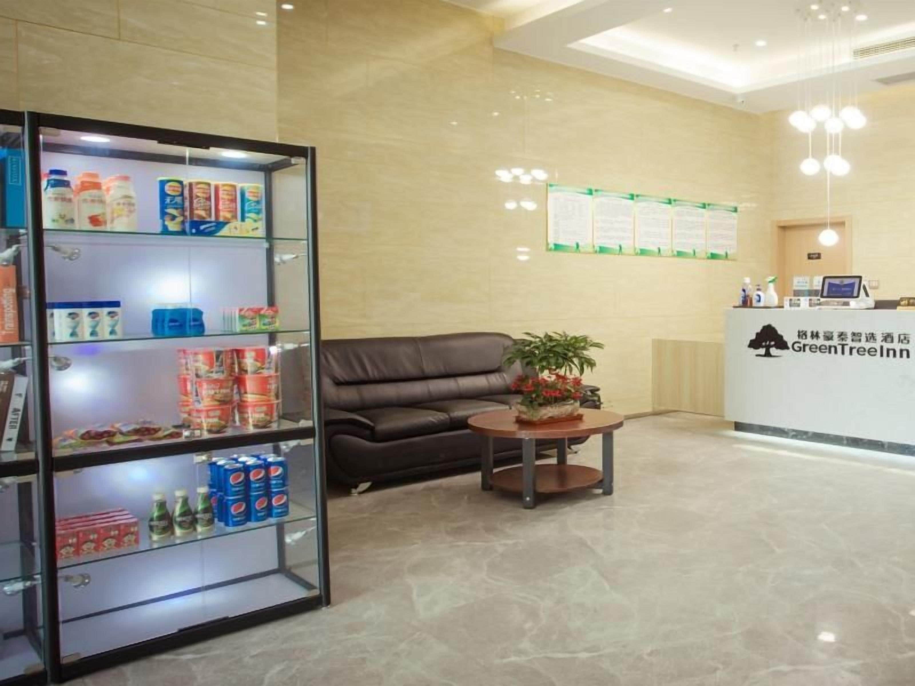 Zona de recepción de un hotel con mostrador de recepción, área de estar con sofá y mesa de centro, y una vitrina de vidrio con diversos artículos.