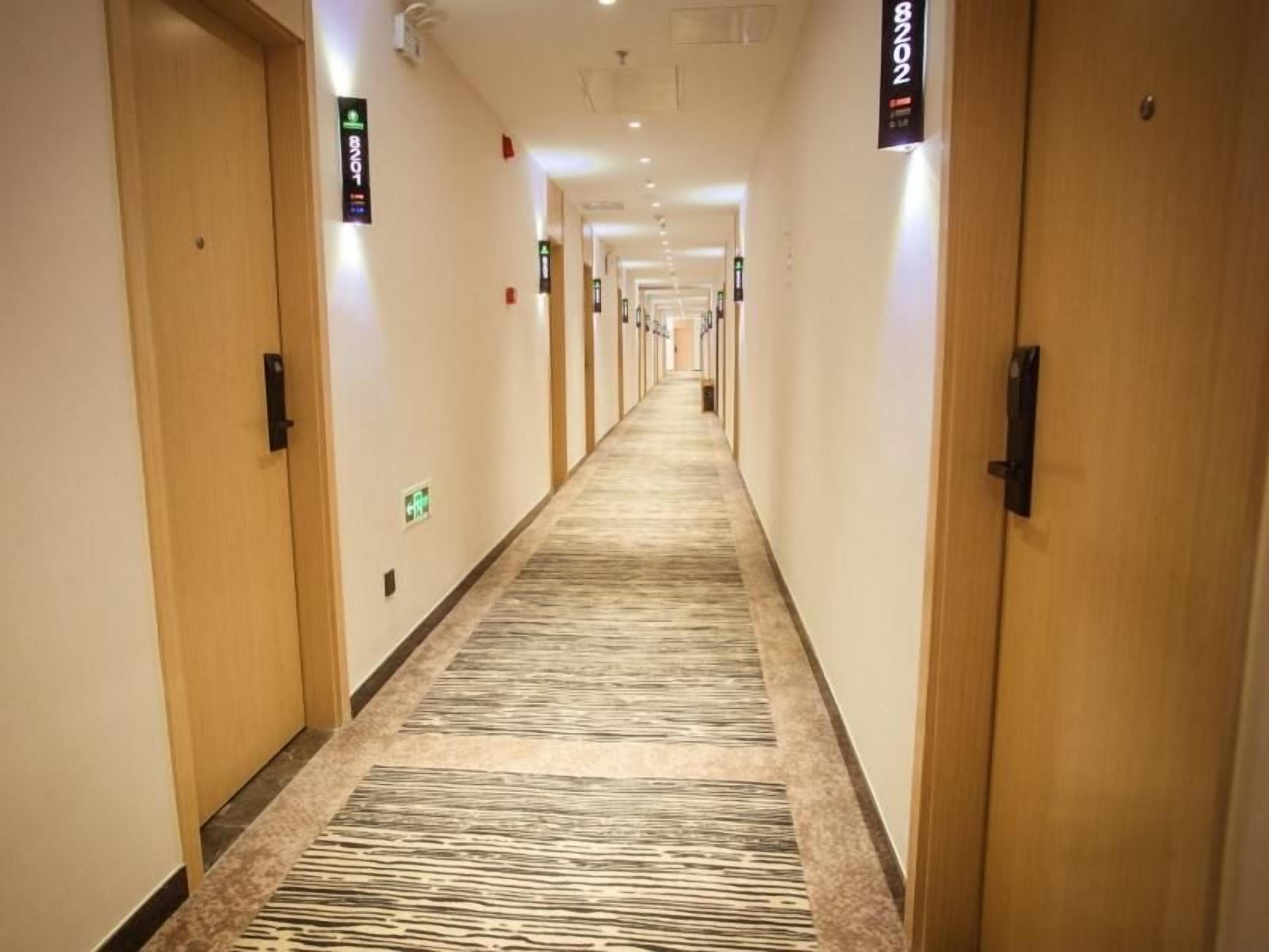 A hotel corridor with doors on both sides, carpeted floor, and overhead lighting.