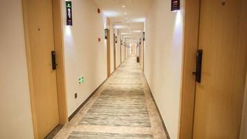 A hotel corridor with doors on both sides, carpeted floor, and overhead lighting.