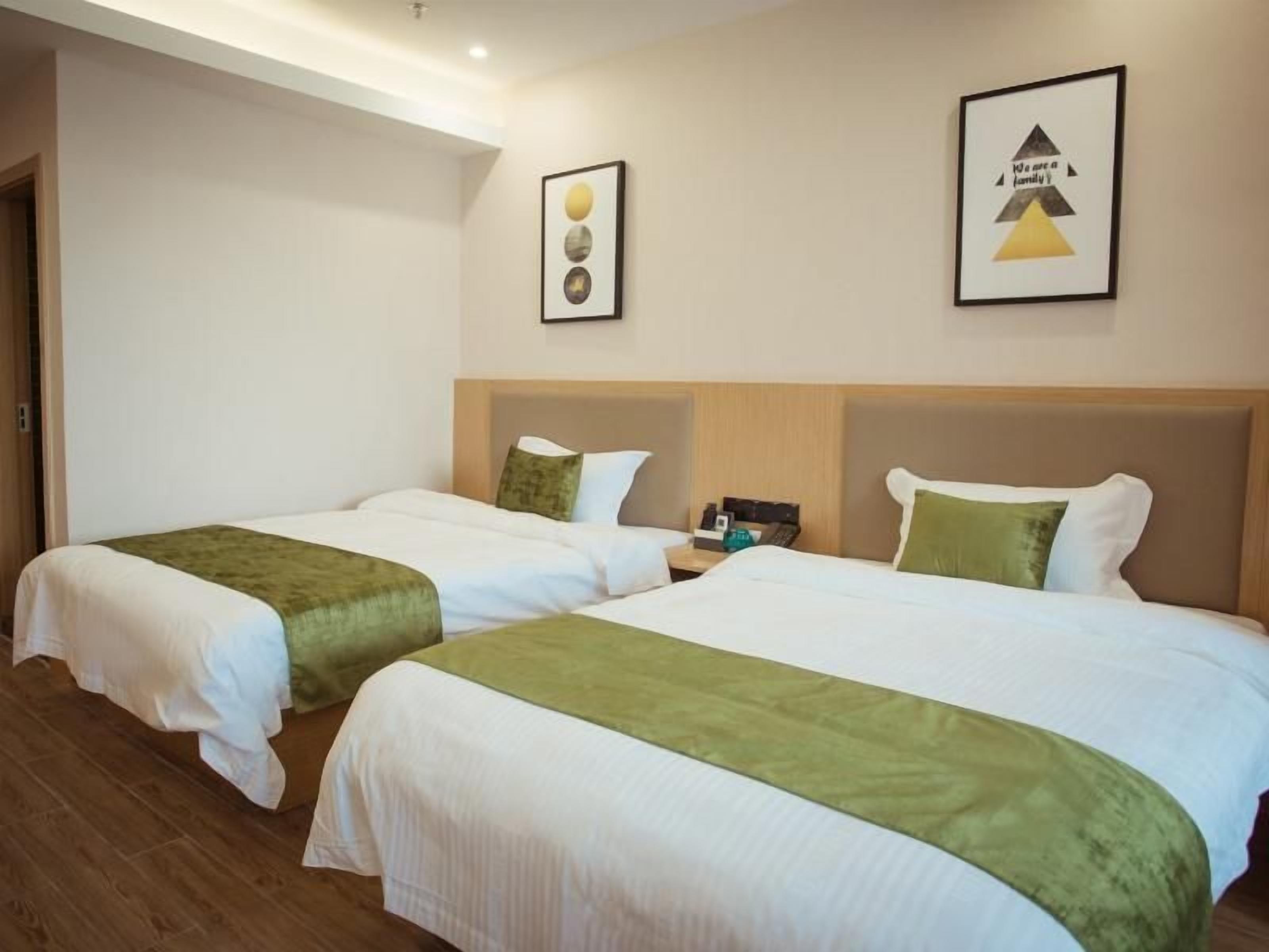 A hotel room with two beds, a wooden floor, and a wall with framed pictures.