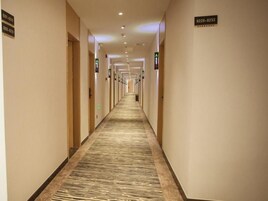 Un pasillo de hotel con pisos alfombrados, puertas a ambos lados y señalización direccional.