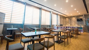 Un restaurante con varias mesas y sillas, amplias ventanas con persianas y una zona de bar con distintos electrodomésticos.