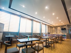 A restaurant with multiple tables and chairs, large windows with blinds, and a bar area with various appliances. - Chonpines Hotel (Shenzhen)