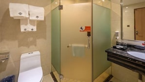 Un baño de hotel con ducha acristalada, inodoro y lavamanos con espejo.