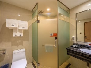 A hotel bathroom with a glass-enclosed shower, a toilet, and a sink with a mirror. - Chonpines Hotel (Shenzhen)