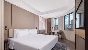 A modern hotel room with a large bed, a desk, and a view of the city through large windows. - Atour Light (Zhuhai)