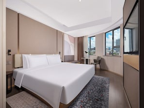 A modern hotel room with a large bed, a desk, and a view of the city through large windows. - Atour Light (Zhuhai)