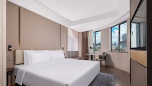 Ein modernes Hotelzimmer mit einem großen Bett, einem Schreibtisch und Blick auf die Stadt durch große Fenster.
