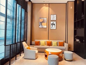 A modern living room with a sofa, armchairs, and a coffee table. There are large windows on one side and artwork on the wall. - Rezen V Hotel Wuxi Yangming Subway Station (Wuxi)