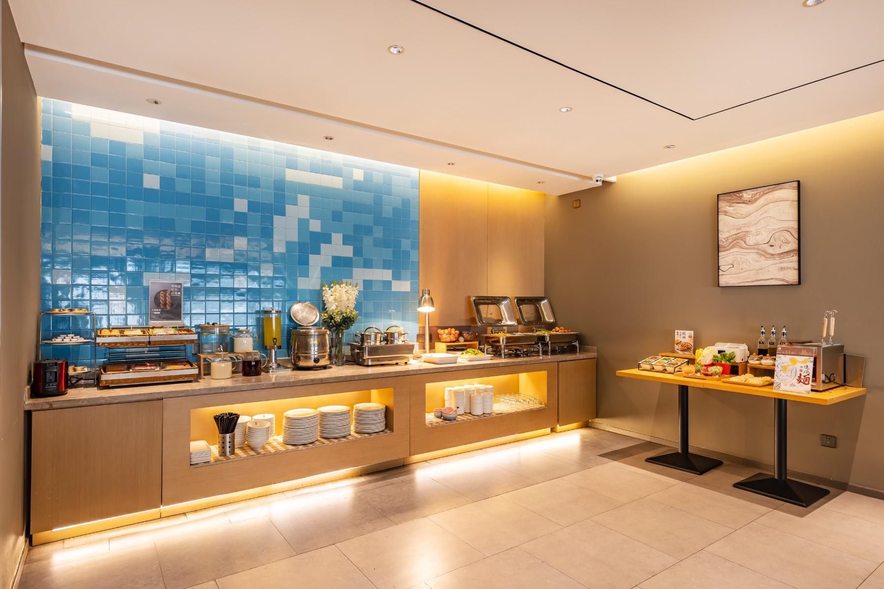 A modern hotel lobby with a reception desk, buffet area, and a large window with blue-tiled walls.
