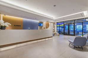 A hotel reception area with a reception desk, seating area, and large windows offering a view of the outside. - Home Inn (Tianjin)