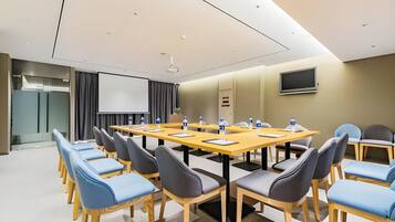 A conference room with a long table, chairs, a projector screen, and a television on the wall.
