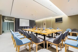 Una sala de conferències amb una taula llarga, cadires, una pantalla de projector i una televisió penjada a la paret.