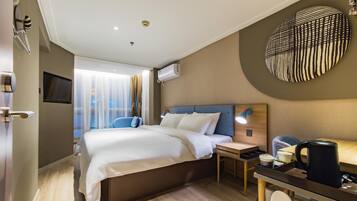 A hotel room with a bed, bedside table, lamp, and a wall-mounted TV.