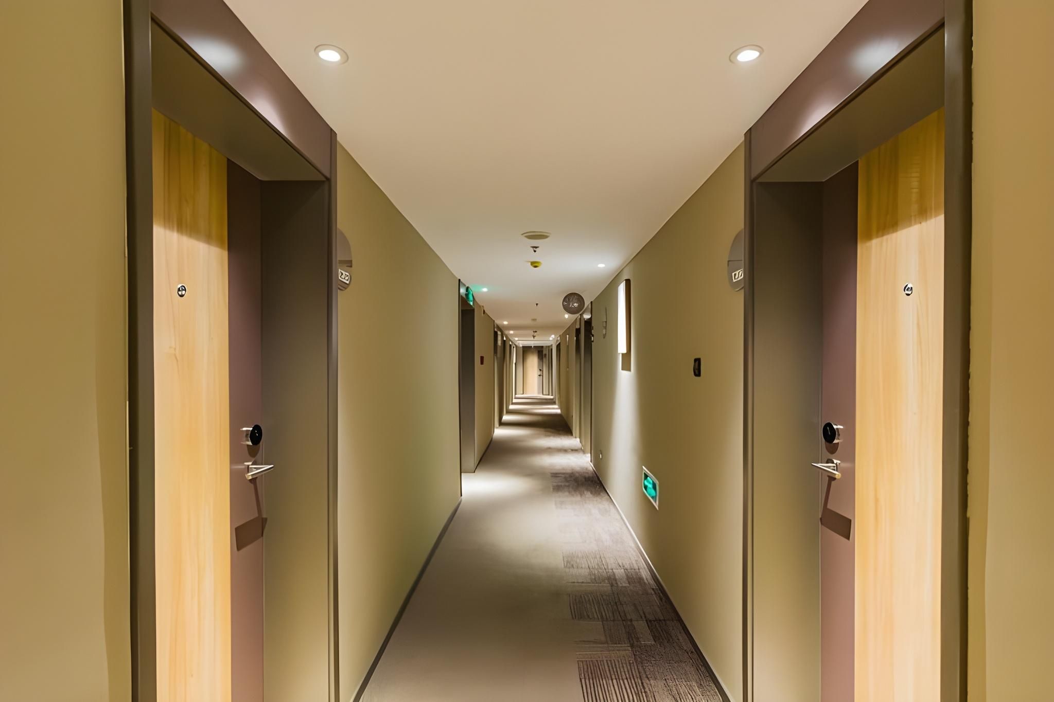 A hotel corridor with doors on both sides, a carpeted floor, and a ceiling with recessed lighting.